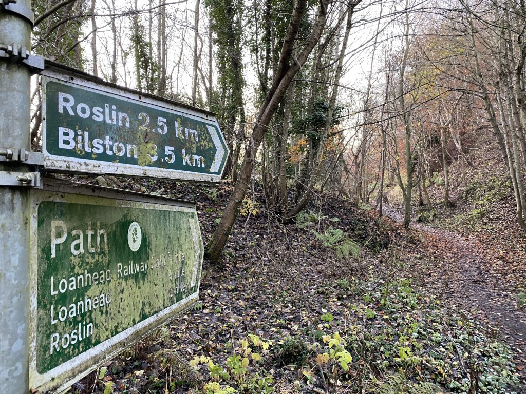 Two dirty path signs pointing towards Roslin and Bilston
