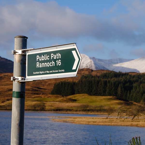 A fingerposts points to the right infant of a loch and snow covered mountains