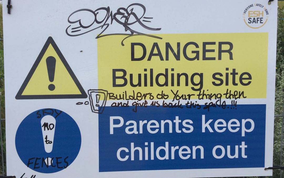 A defaced health and safety sign on fencing saying "hurry up and give us our space back"
