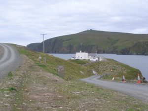 The former shore station at Burra Firth, now the Hermaness National Nature Reserve Visitor Centre, with RAF Saxa Vord behind. The path to the left leads to the top of Hermaness Hill. © UK Payphone Directory, Geograph