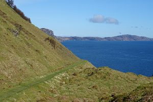 NG598376: track descends gently towards a bend at Gualann na Leac. In the distance is the north of Raasay, between Brochel and Arnish. You can see Brochel from here, at the left extremity of the sea, but it's not obvious in this small image (2018). © Anne Burgess, Geograph